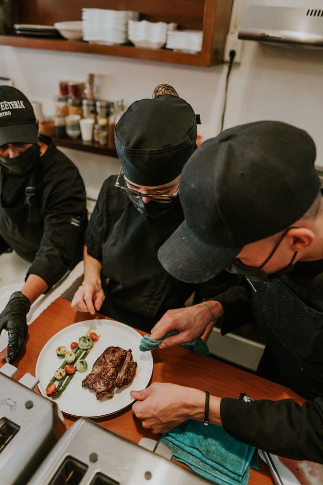 Cooks in caps and masks plating food in a small kitchen