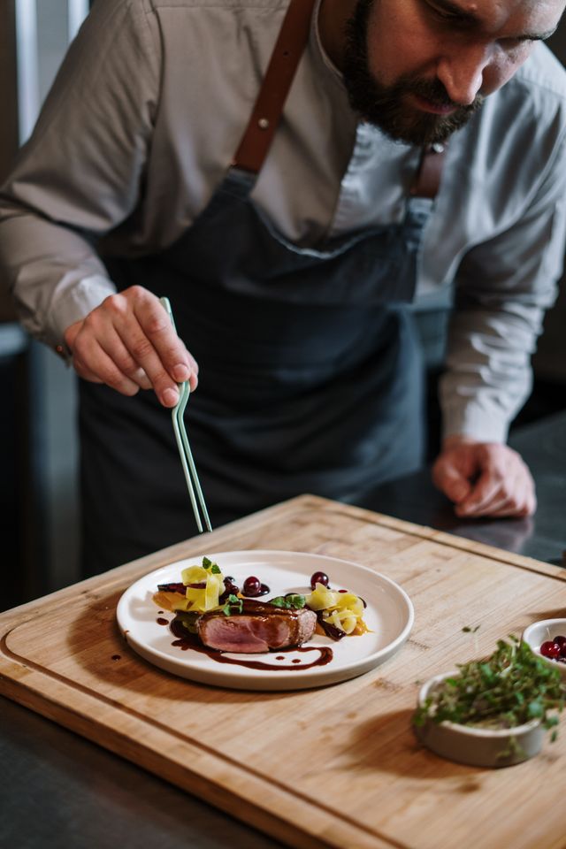 A chef carefully finishing a plated dish with herbs