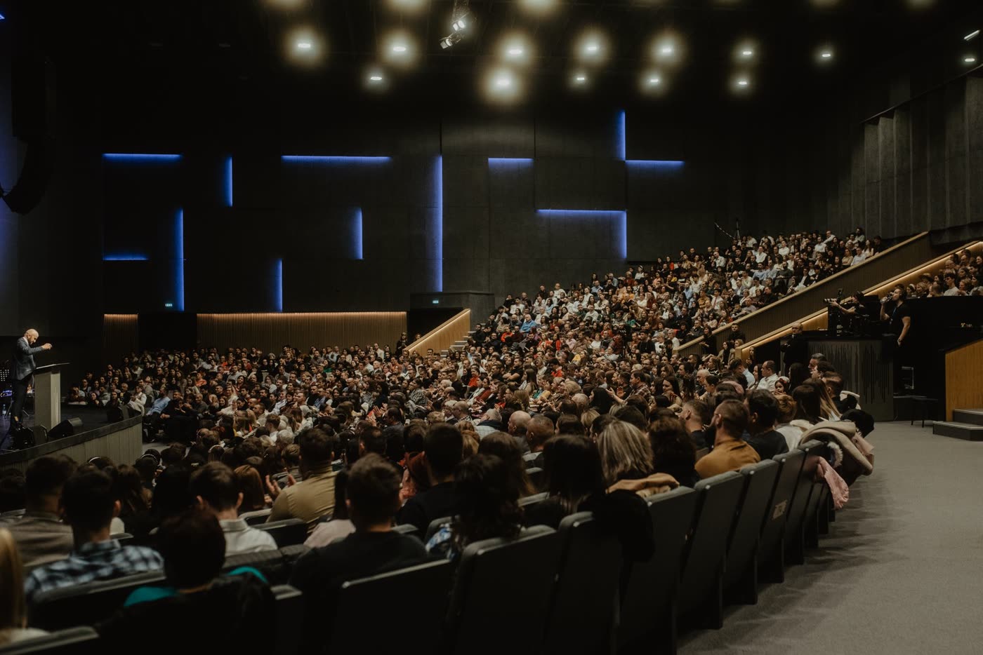 A full auditorium facing a stage with blue light strips