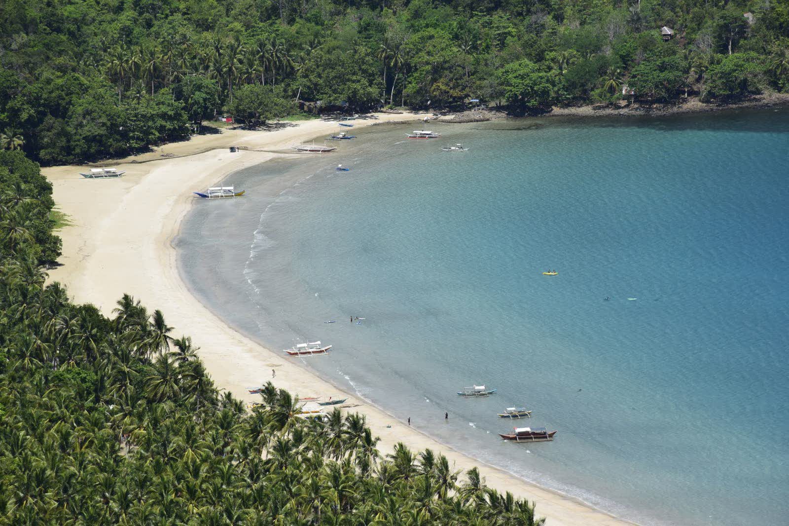 A quiet white-sand cove with clear water and green hills