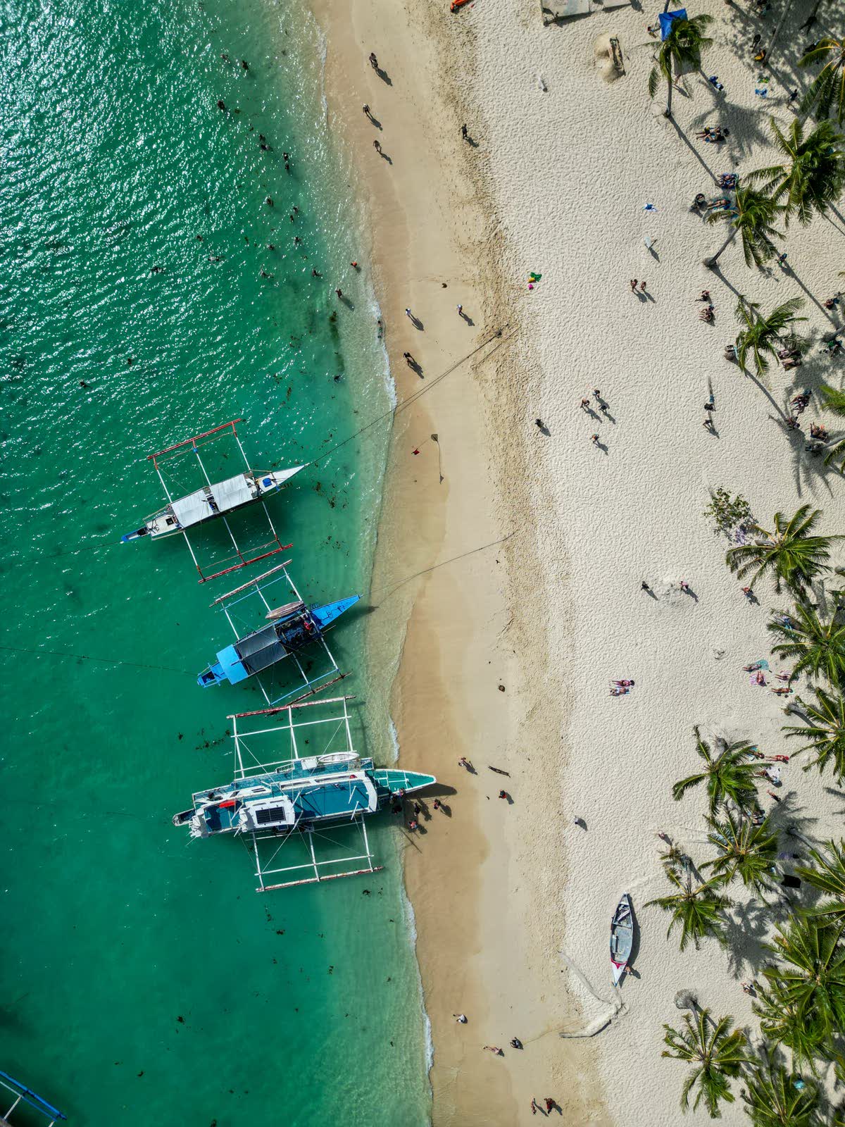 Aerial view of a curving beach with outrigger boats pulled up on the sand