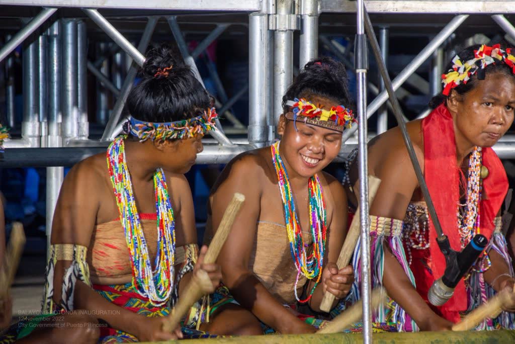 Indigenous performers in beaded headbands and necklaces playing bamboo instruments