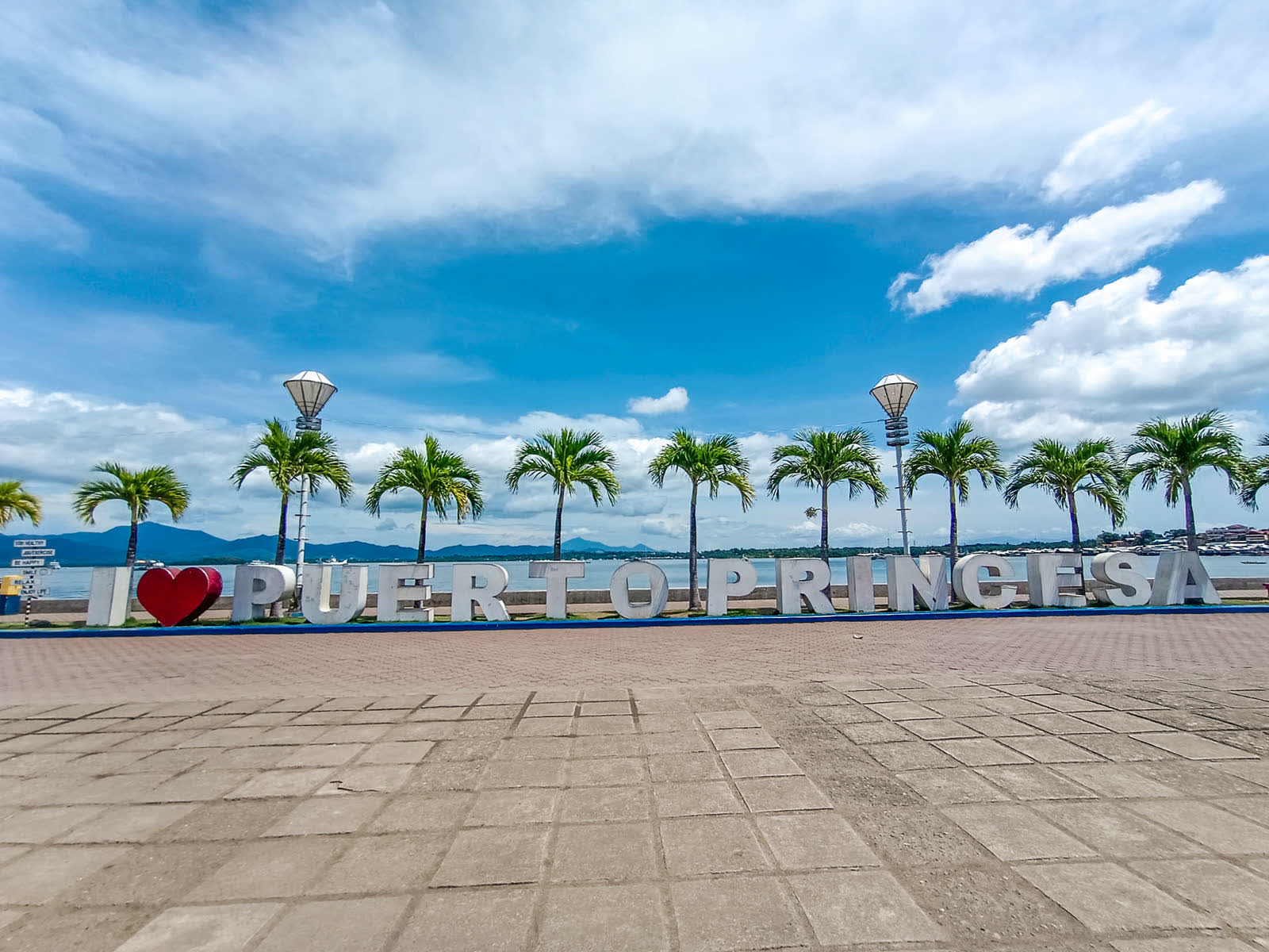 Palm trees and the I love Puerto Princesa sign along the Baywalk under a blue sky