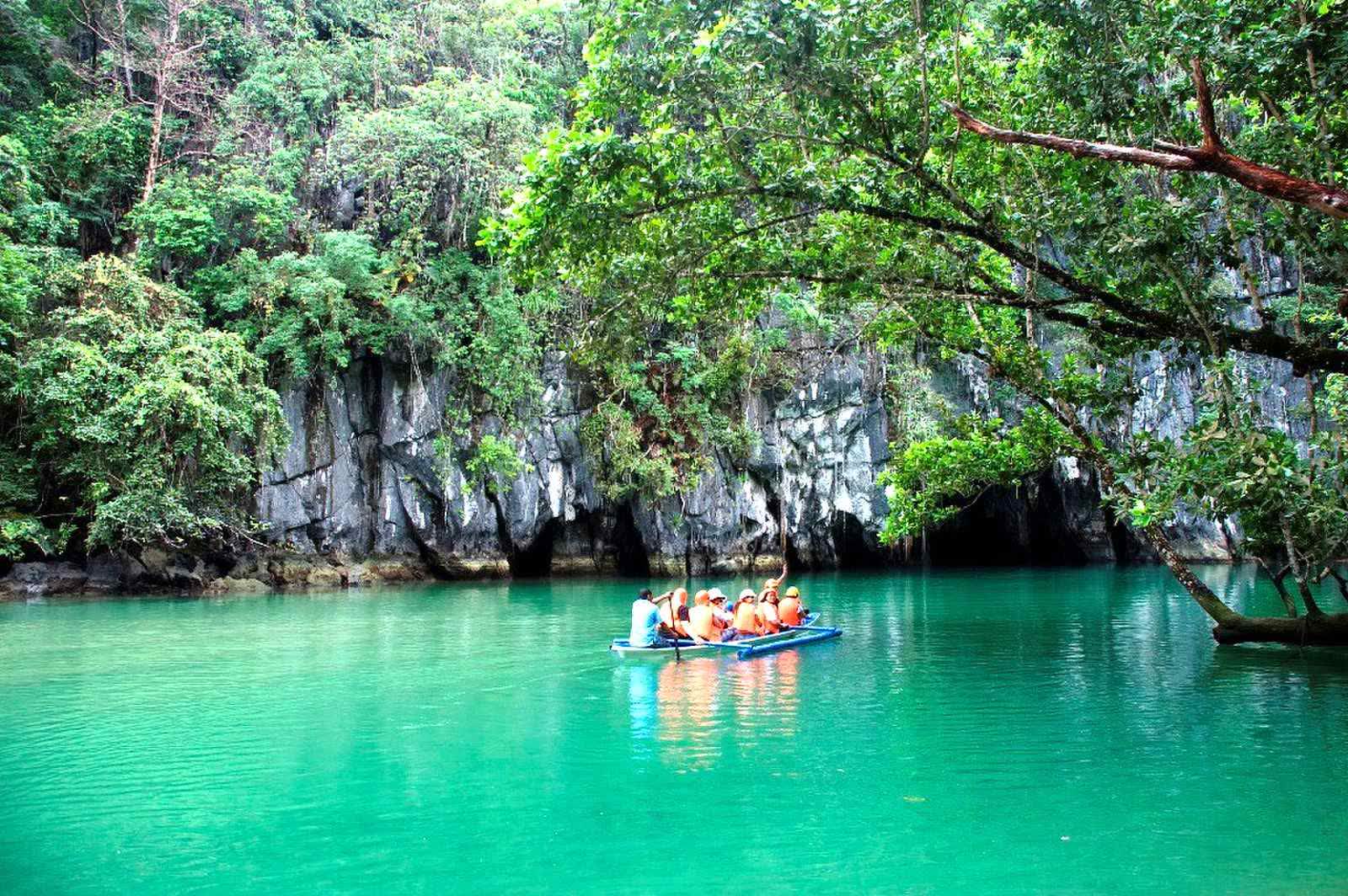 A tour boat on turquoise water below limestone cliffs at the mouth of the Underground River