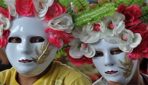 Two festival-goers in white masks crowned with red and white paper flowers