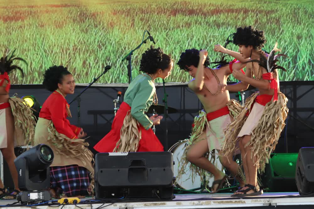Performers in red and woven costumes dancing on a stage