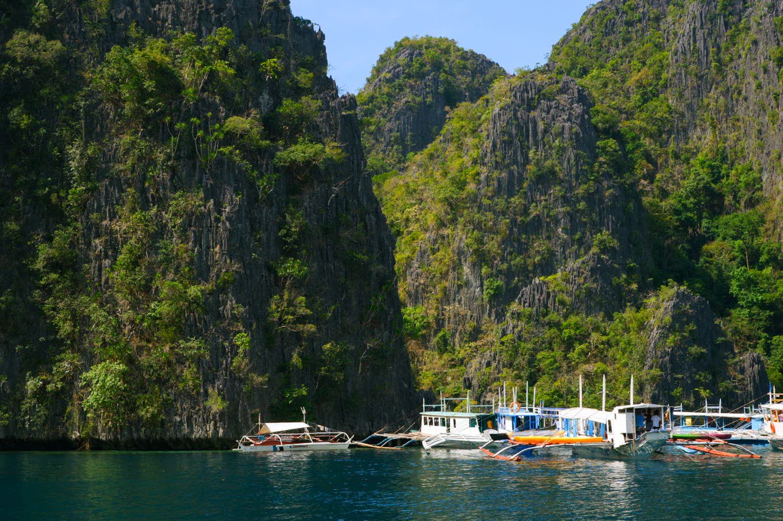 Tour boats anchored below sheer limestone cliffs