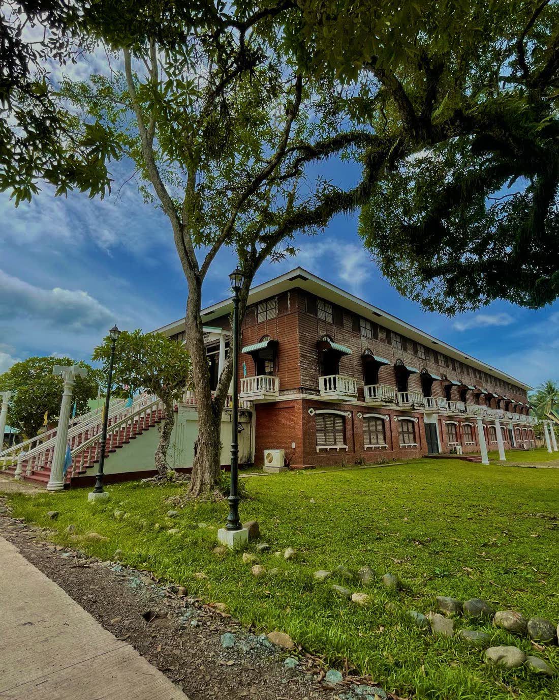 A long two-storey red-brick colonial building with a grand staircase and lawn
