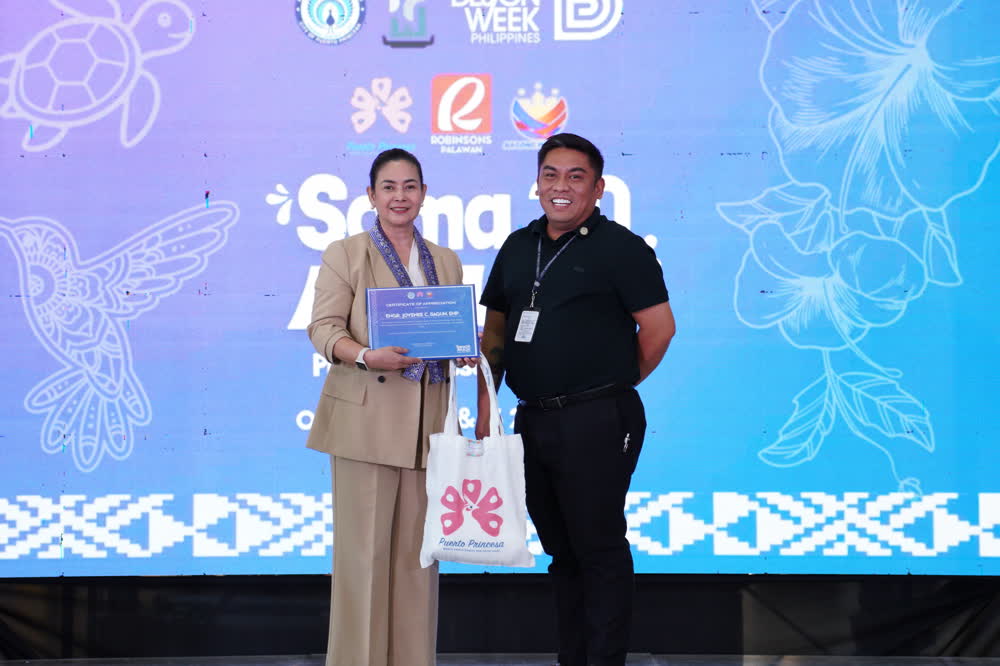 Two people holding a certificate on a stage decorated with Palawan motifs