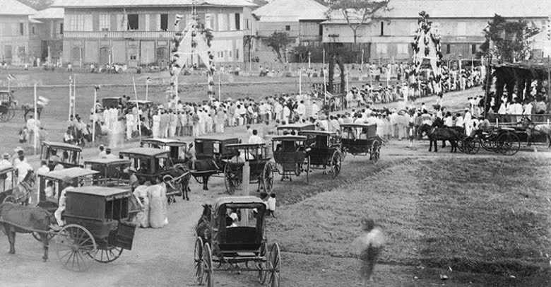 An archival black and white photograph of horse-drawn carriages on a town street