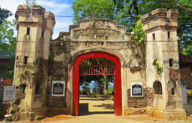 The restored stone gate of Plaza Cuartel with a red arch, under trees