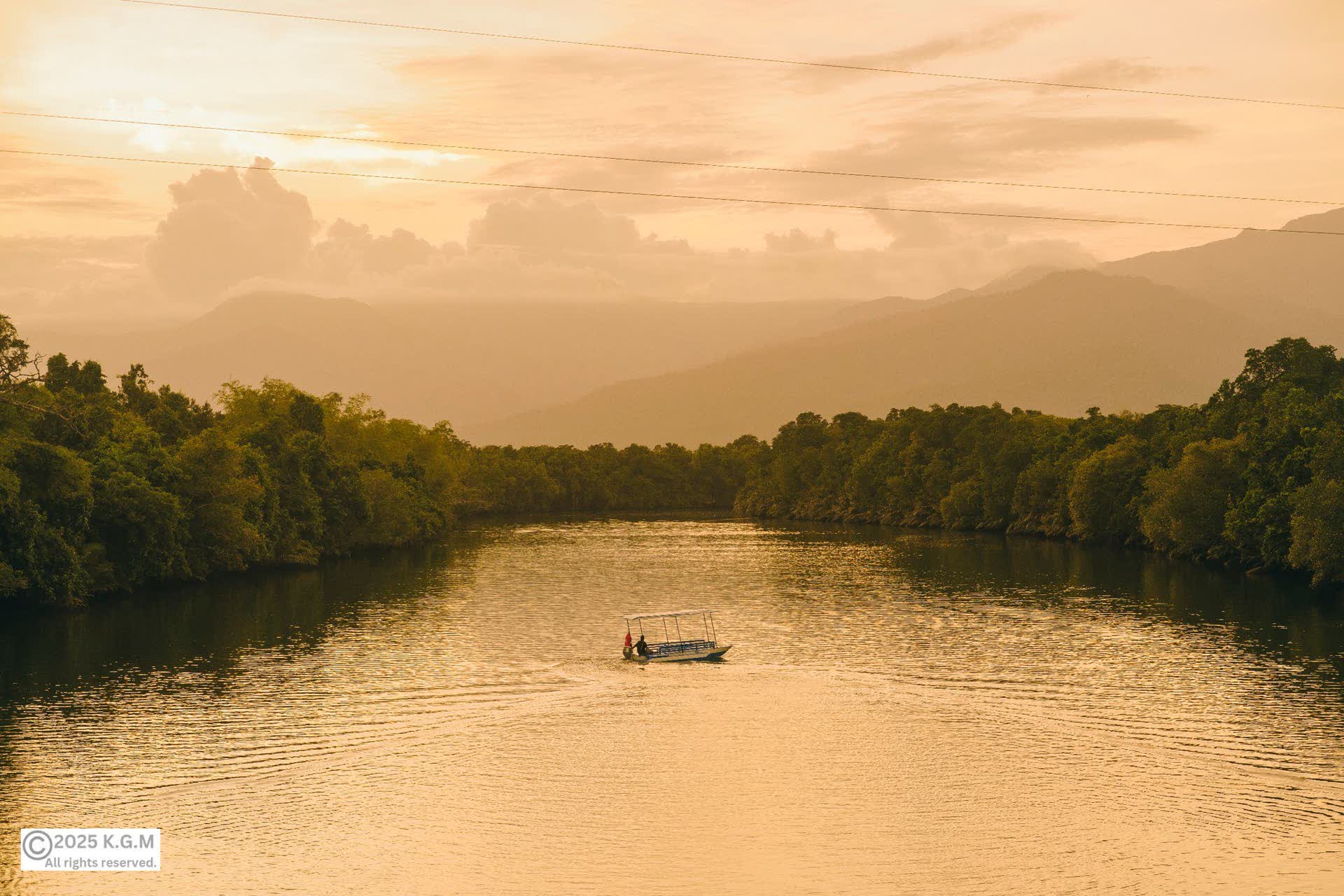 A lone boat on a wide river at golden dusk, forest on both banks