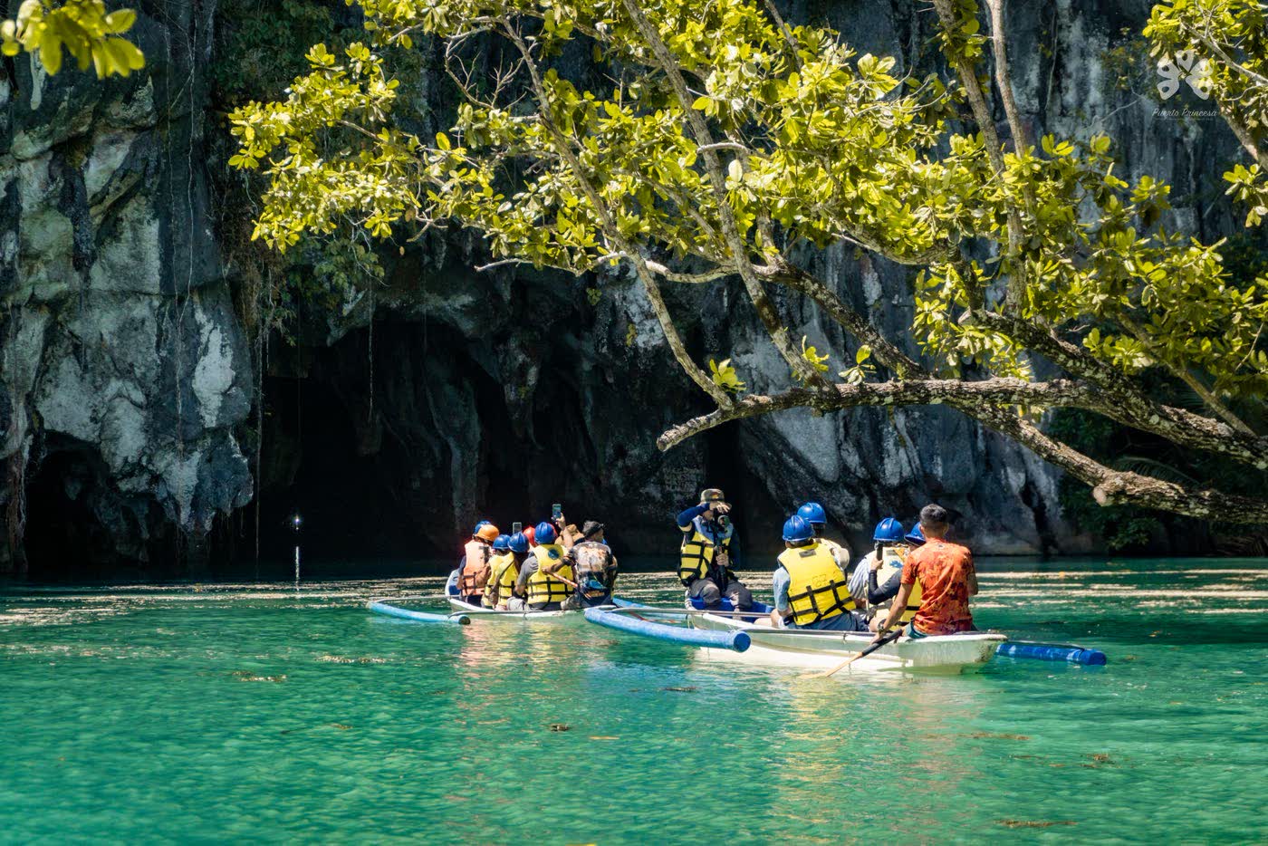 Paddle boats of visitors on turquoise water near the cave entrance