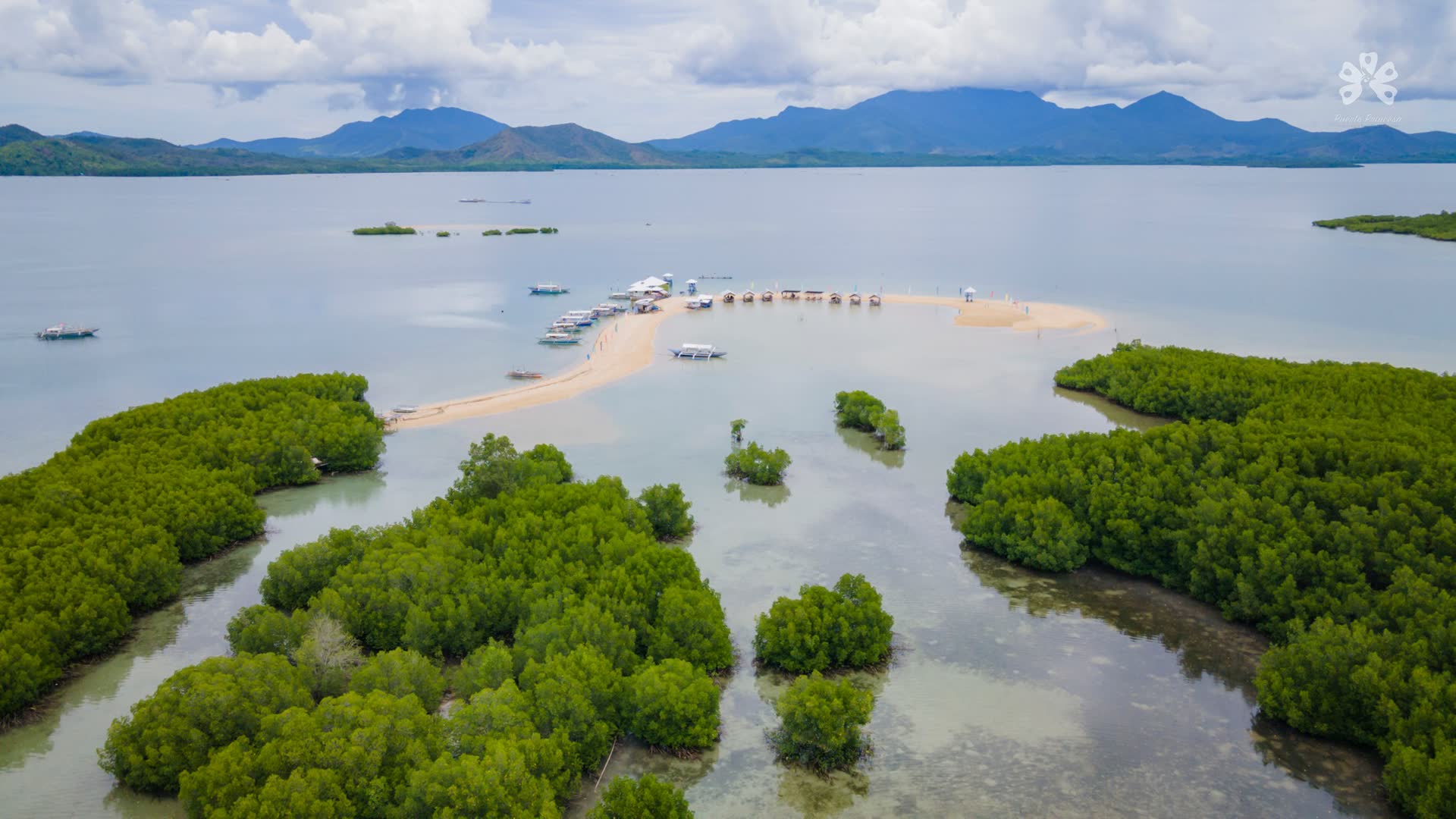Aerial view of a long sandbar and mangrove islets in a calm bay, mountains on the horizon