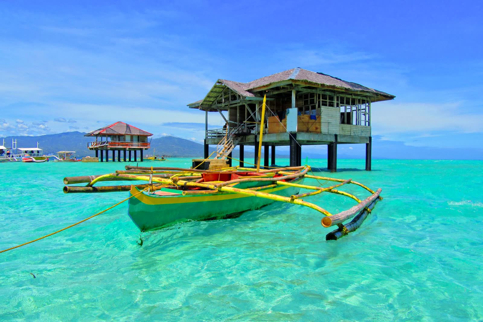 A thatched stilt cottage and an outrigger boat over turquoise water