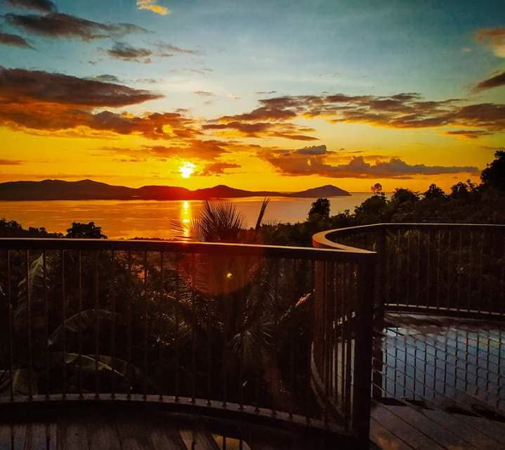 The sun setting over a bay and distant islands, seen from a hillside deck