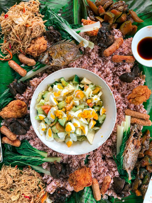 Overhead view of a boodle feast around a bowl of salted egg and tomato salad