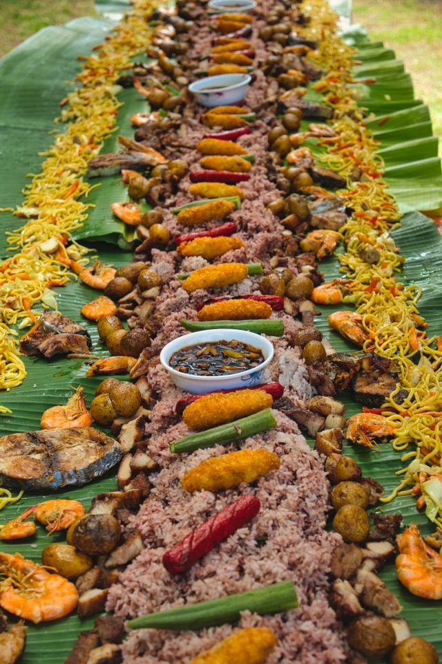 A long boodle fight spread of rice, pancit, grilled fish, shrimp and sausages on banana leaves