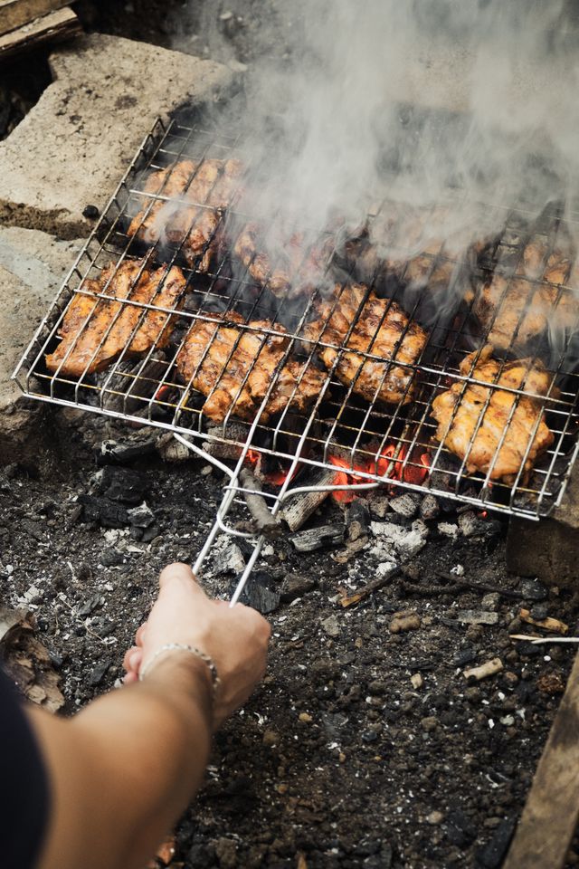 Chicken grilling over glowing charcoal with smoke rising