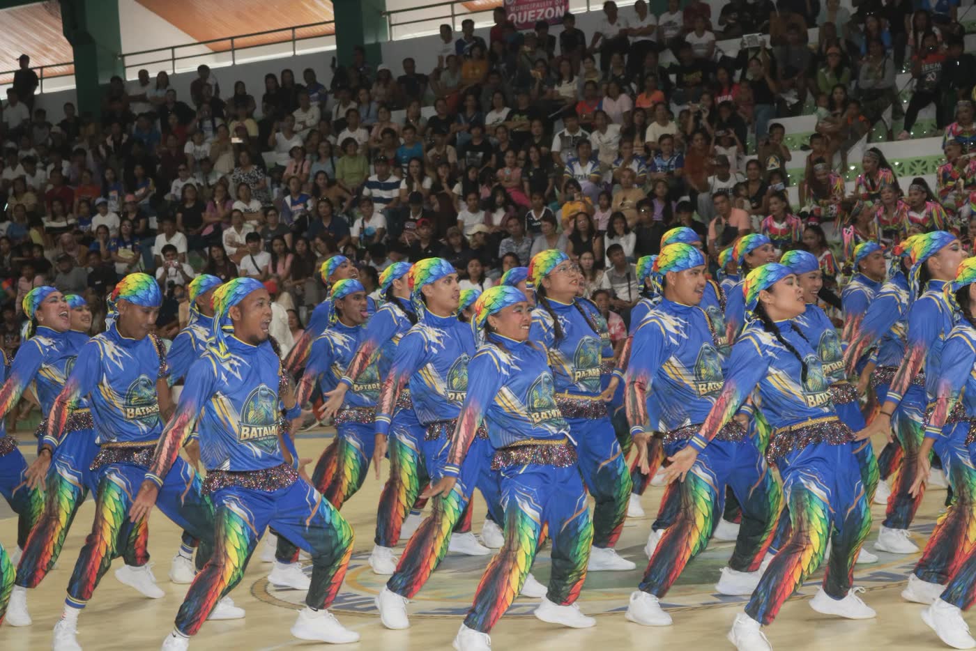 A dance troupe in blue and rainbow costumes mid-performance