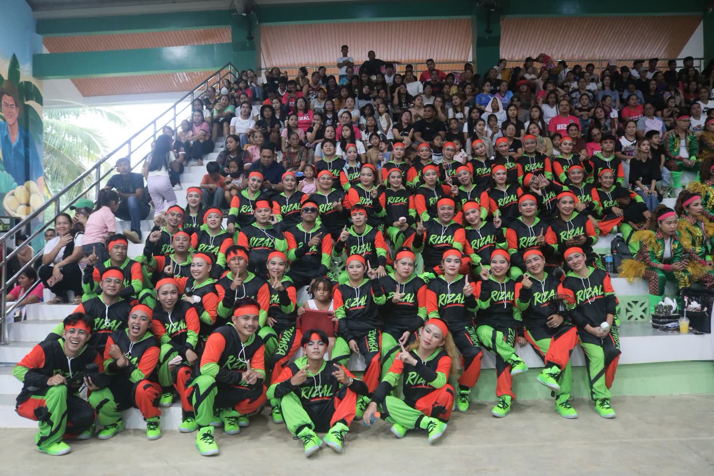 Dancers in green and black costumes seated together in the stands