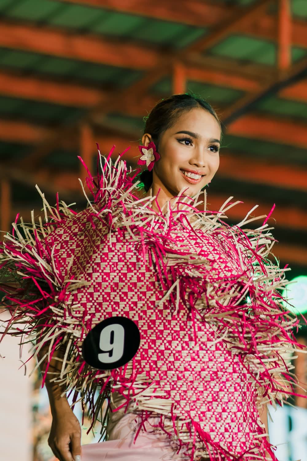 A smiling young woman in a gown woven from red and pink fibres on stage