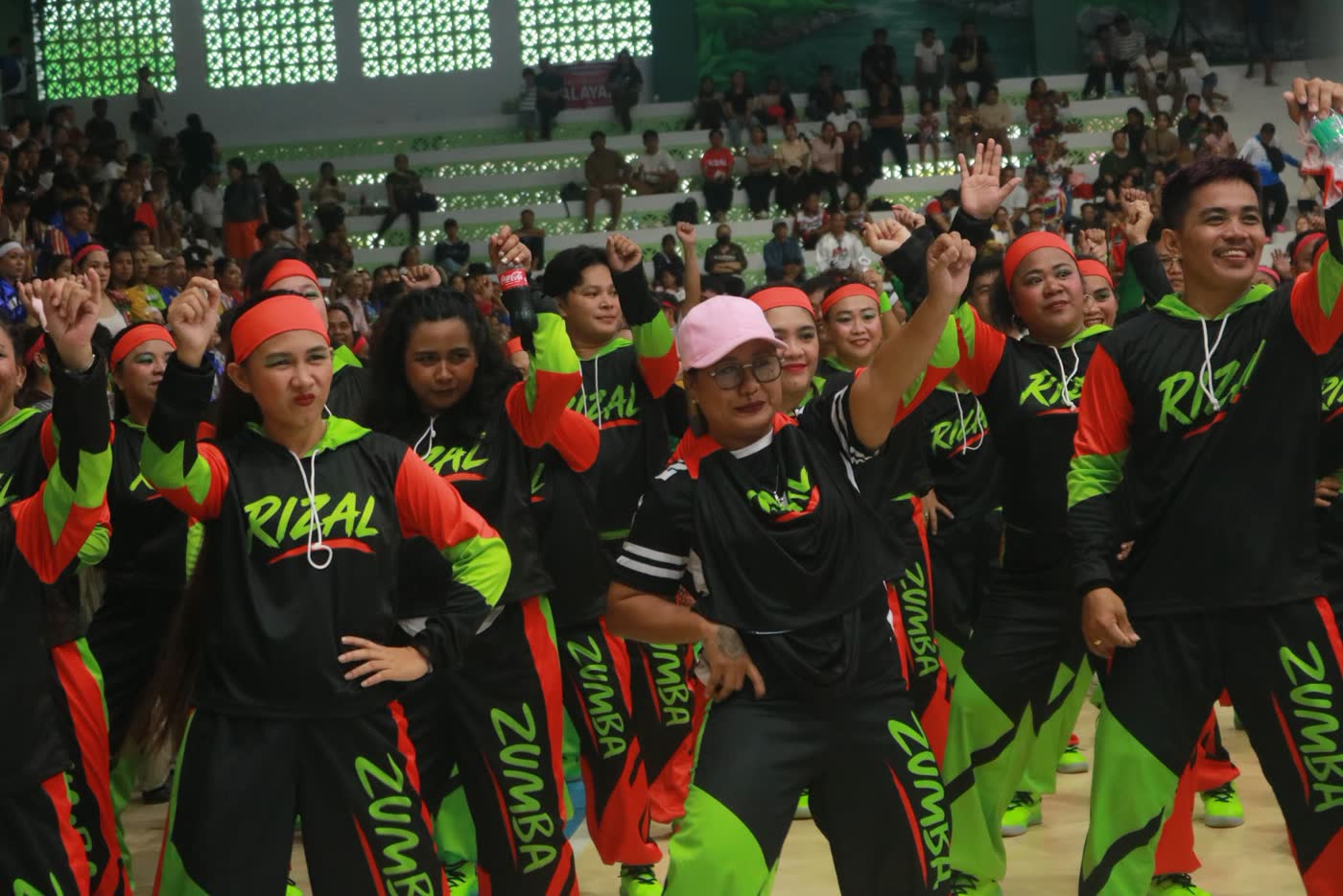 Dancers in black and neon green Rizal shirts cheering in a gym