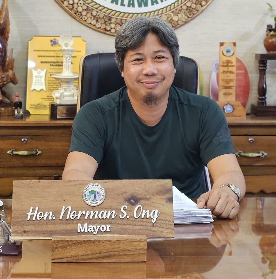 Mayor Norman S. Ong seated at his desk with a nameplate, plaques behind him