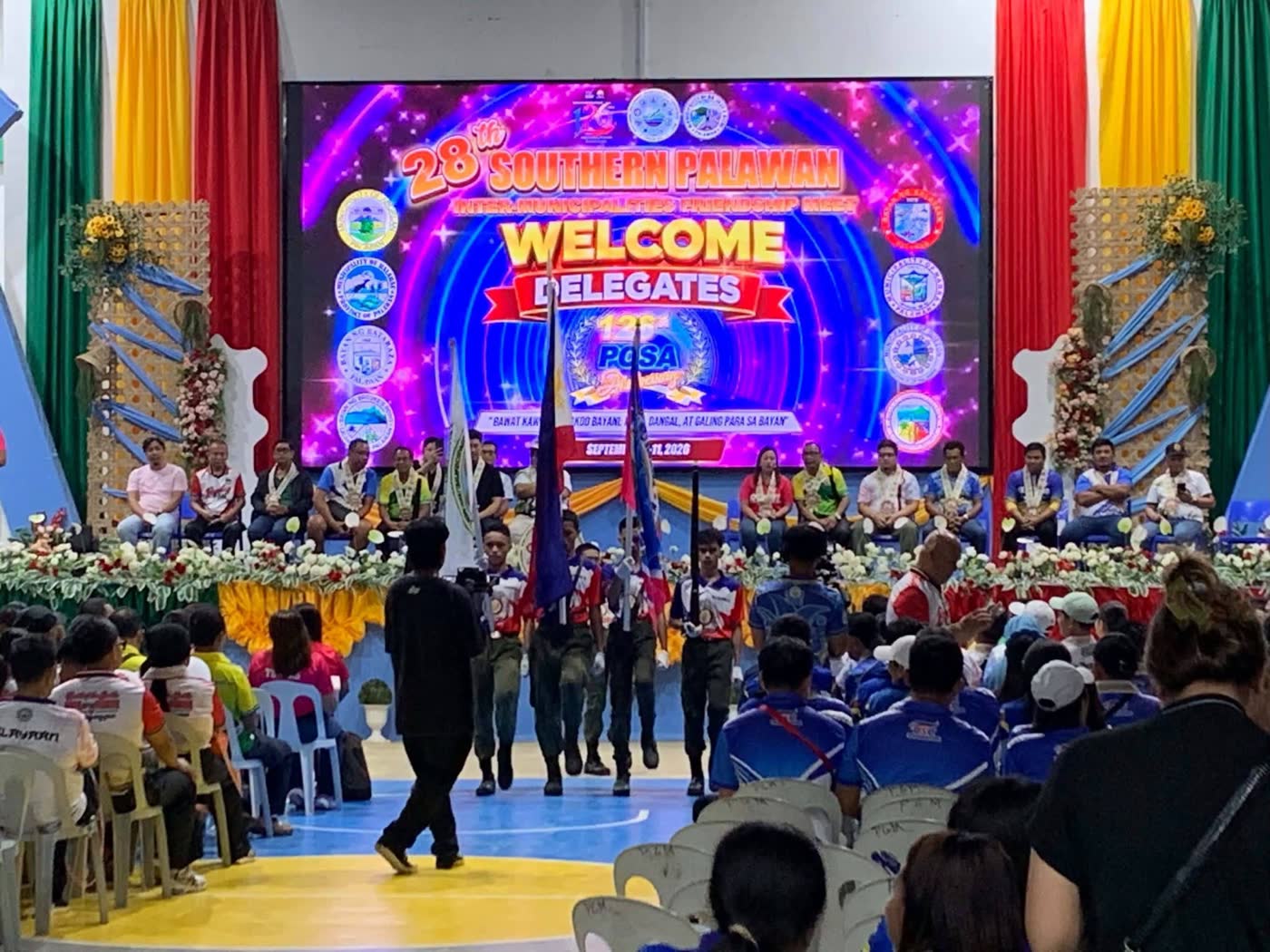 Delegations seated before a stage with a large screen welcoming delegates to the 28th Southern Palawan meet