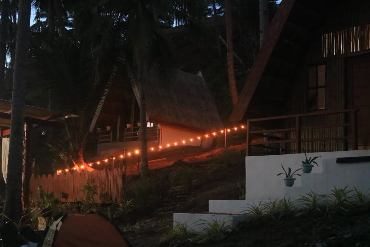 Cottages on a hillside at dusk, lit by strings of warm lights