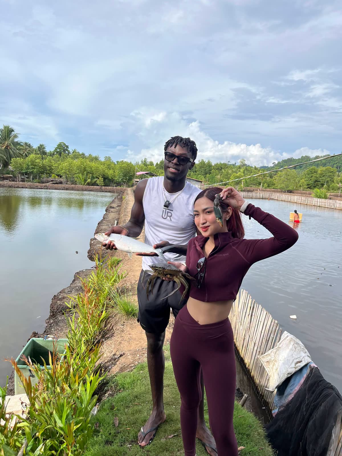 Two visitors holding up a fish on the dike of a fishpond