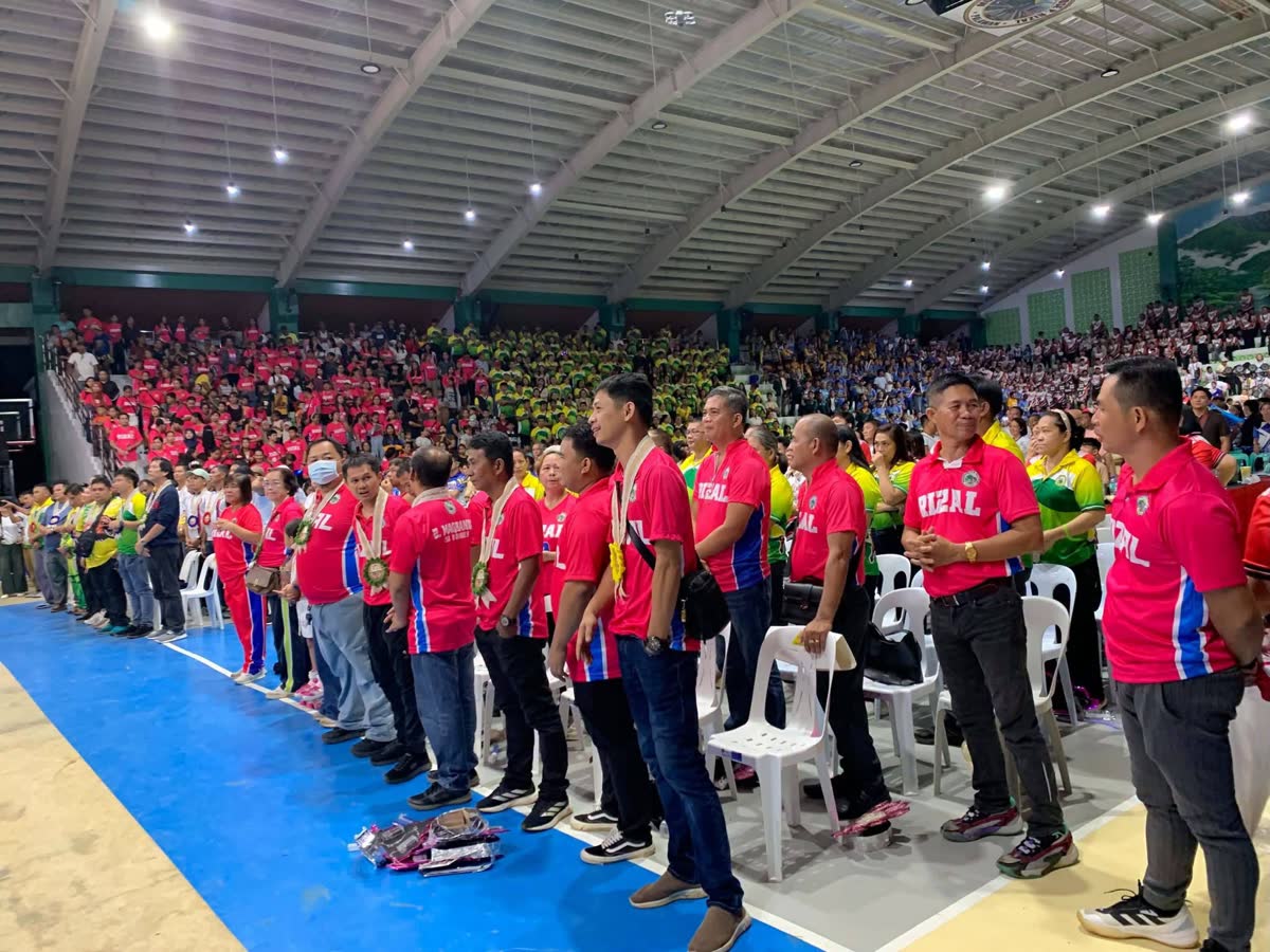 Athletes in red jerseys lined up before packed stands in a gymnasium