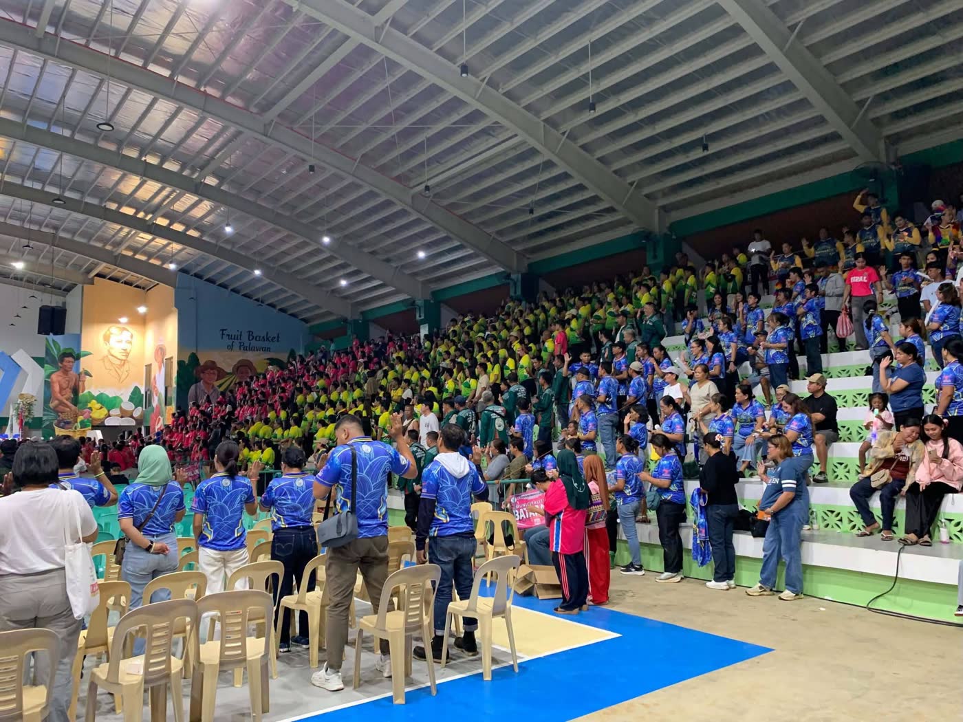 Athletes in red uniforms lined up in a gymnasium for an opening ceremony