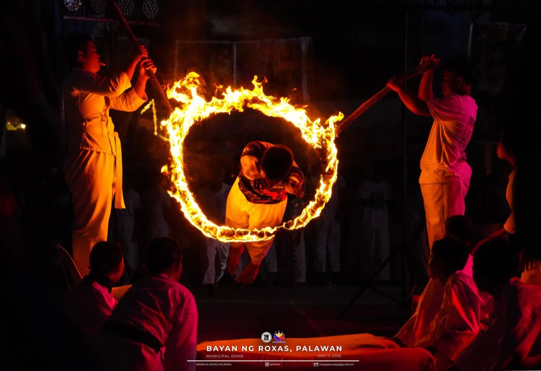 A performer leaping through a ring of fire held by two others