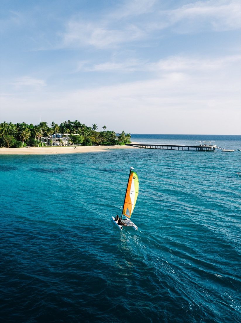A catamaran sailing on turquoise water near the island
