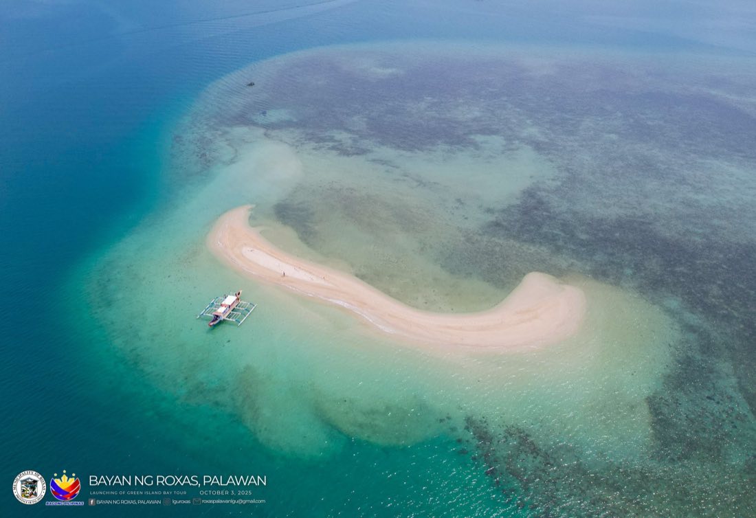 A crescent-shaped sandbar in clear shallows with a bangka