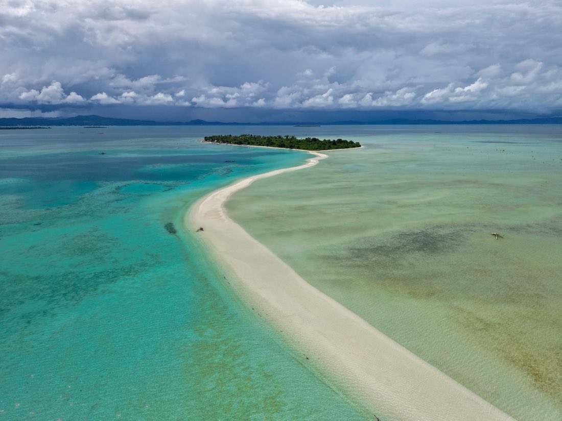 A long white sandbar curving to a small wooded island