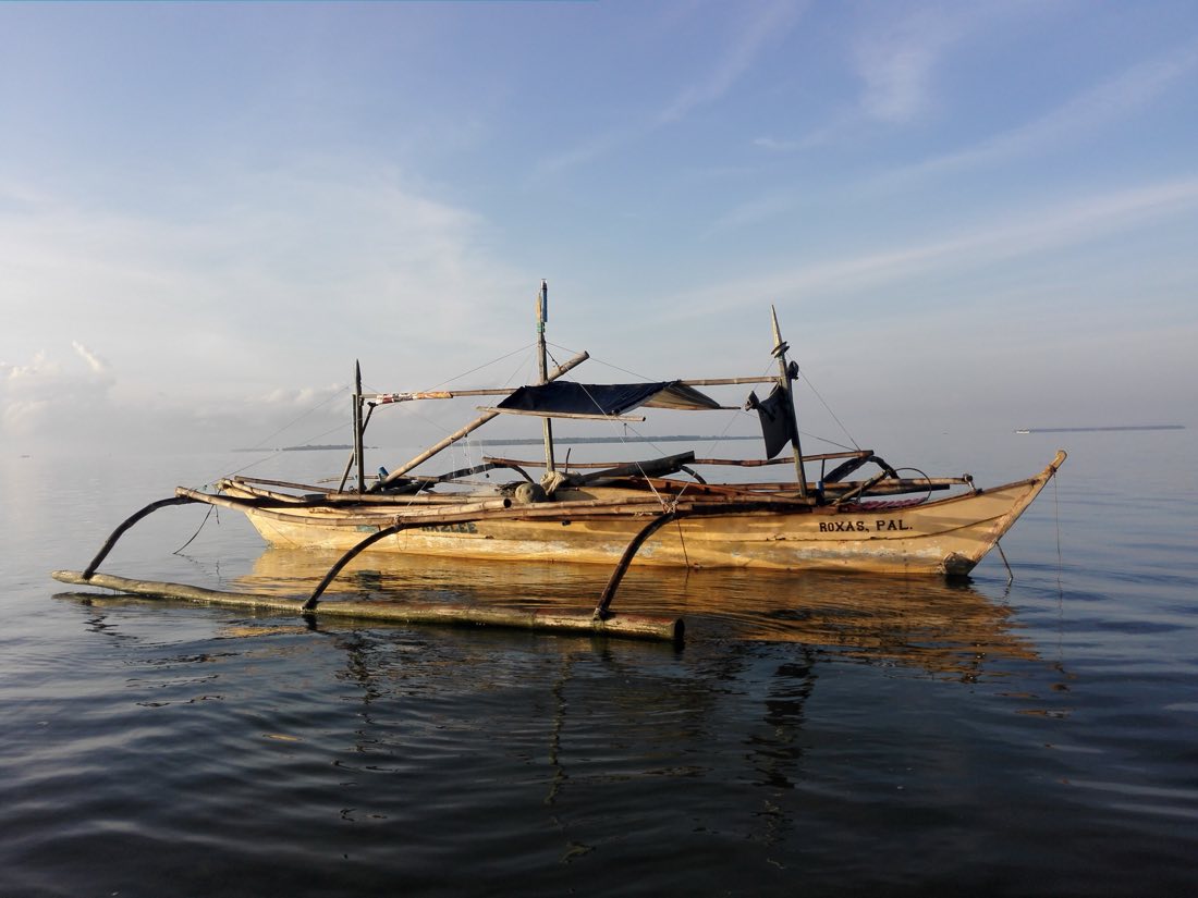 A wooden outrigger boat anchored on calm water