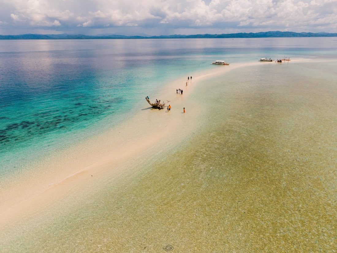 People walking along a long sandbar that runs out to sea