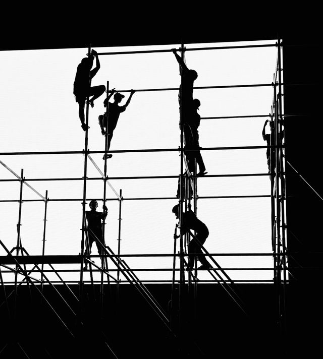 Silhouettes of a crew climbing scaffolding against the sky