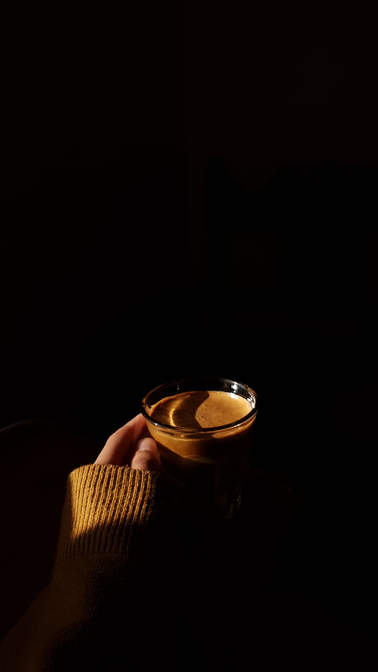 A hand holding a glass of coffee in warm evening light